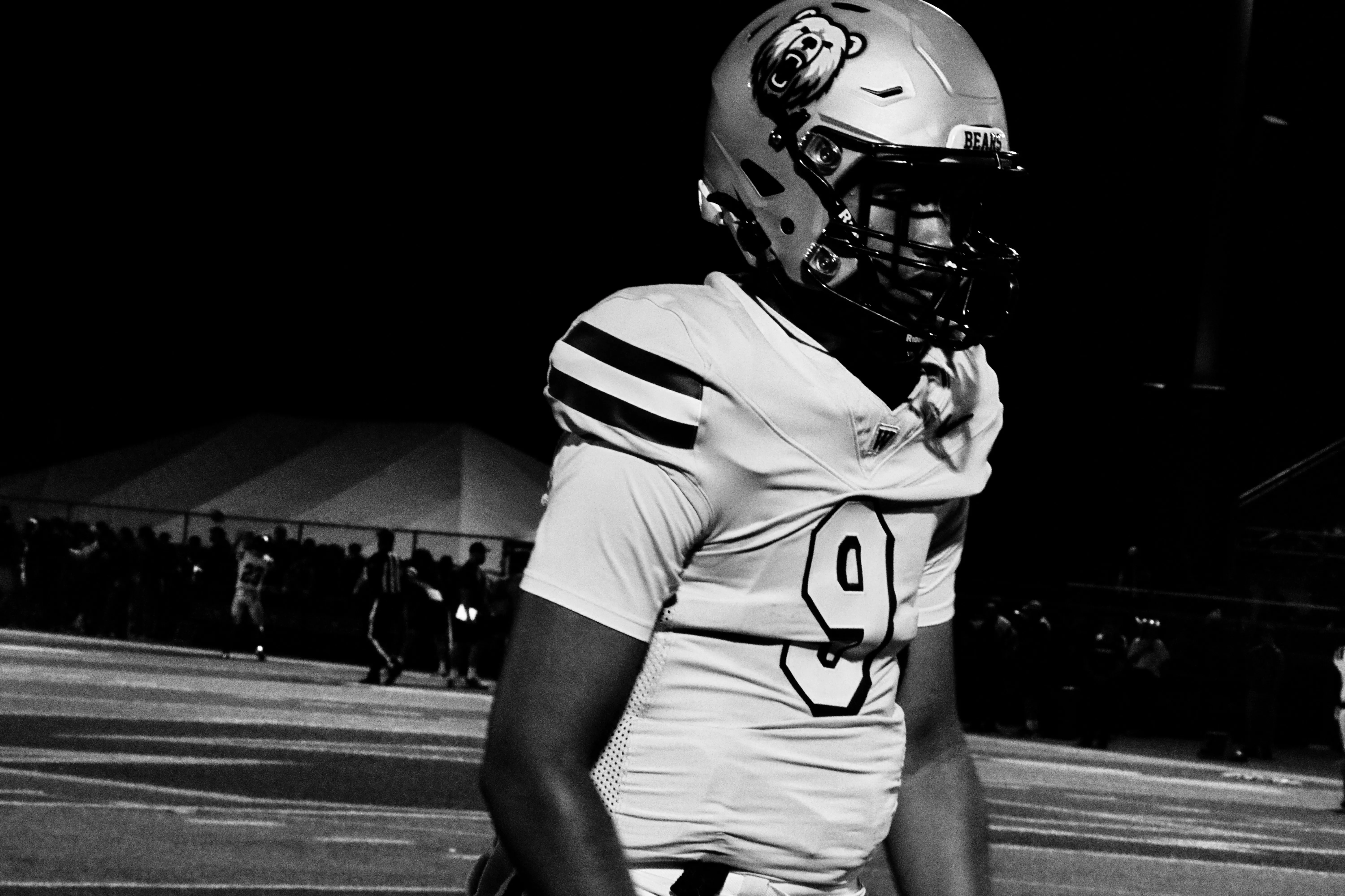 Black-and-white photo of a Warren Bears player wearing number 9 walking the field at night, fans along the fence in the background.